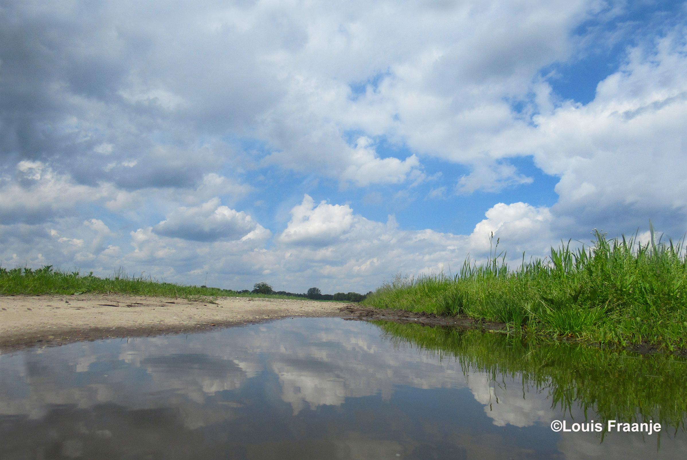 Een waterplas op het landweggetje geeft een mooie weerspiegeling van de wolken - Foto: ©Louis Fraanje