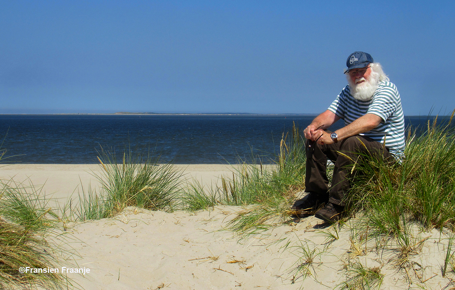 Louis zit heerlijk op een duintop aan de zee en aan de overkant zie je het eiland Vlieland liggen - Foto: ©Fransien Fraanje