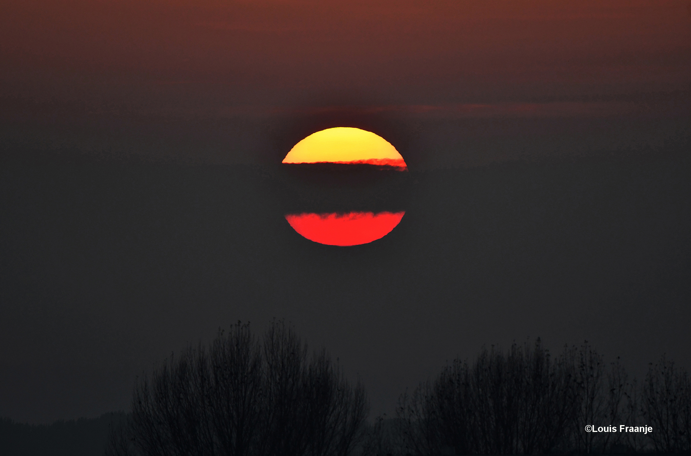 De avondzon kwam halverwege haar tocht achter deze wolkenband langs - Foto: ©Louis Fraanje